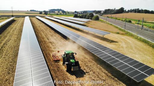 Ein Traktor zieht eine Egge durch eine Agri-PV-Anlage mit einem Tracker-System.