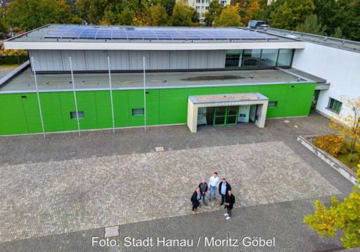 Luftbild mit fünf Personen vor einem öffentlichen Gebäude mit PV.