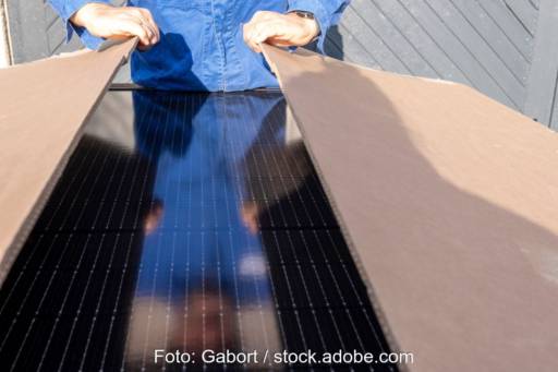 Person im Blaumann öffnet Paket mit Solarmodulen.