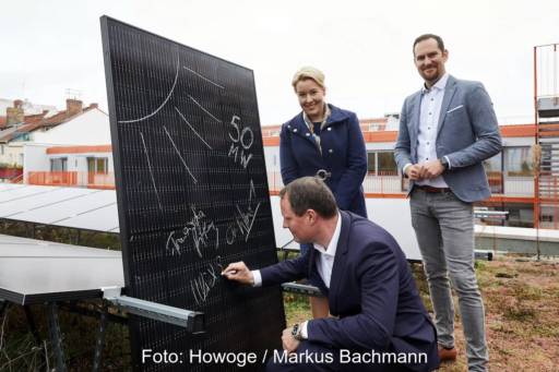 Solarmodul mit gezeichneter Sonne und Unterschriften, ein Mann unterschreibt, eine Frau und ein Mann stehen daneben.