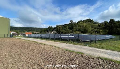 Solarkollektorfeld hinter Zäunen und neben einem Getreidespeicher.