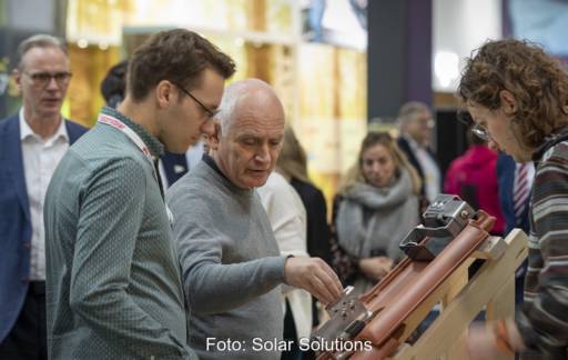 Menschen stehen vor Dachziegel mit Solar-Montage-Set an einem Messestand - Solar Solutions in Düsseldorf