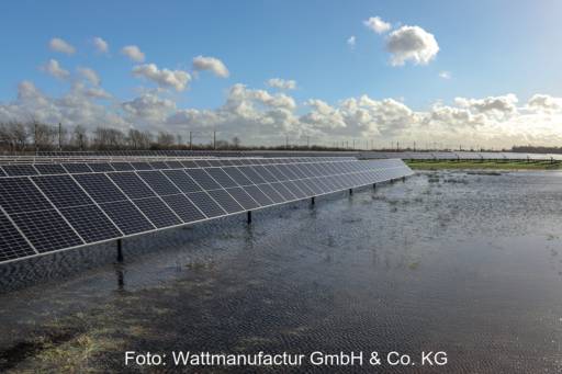 Im Vordergrund eine Wasserfläche in einem wiedervernässten Moor. Links im Bild eine Reihe aufgeständerter Photovoltaik-Module.