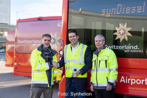 Drei Männer mit gelben Warnwesten vor roten Flughafen-Bussen: Vertrag über Solar-Treibstoff von Synhelion.