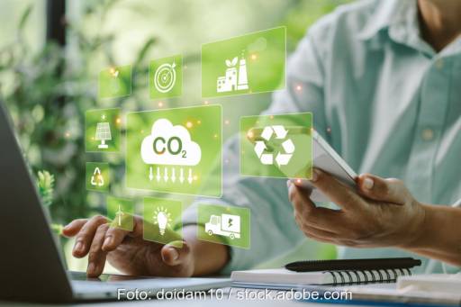 ein Mann tippt am Computer. Dabei schweben Symbole aus dem Klimaschutz virtuell über dem Schreibtisch. Symbolbild für die Kommunalrichtlinie.