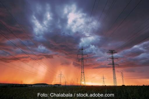Grauer Himmel über Stromnetzen, am Horizont dringt die Sonne durch.