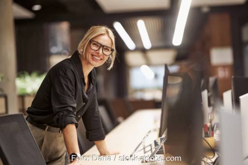 Eine tatkräftige Frau lachend an einem Schreibtisch mit Planungsutensilien.
