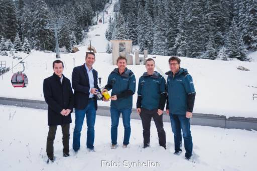 5 Männer an einer Skioiste mit Sessellift und einer Probeflasche mit durchsichtigem solaren Treibstoff.