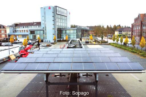 Solarcarport auf einem Parkplatz. Im Hintergrund das Gebäude der Sparkasse.
