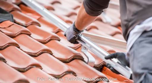 Im Bild eine Hand, die eine Photovoltaik Unterkonstruktion installiert, das ist Sache vom Dachdeckerhandwerk.