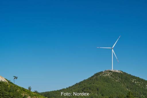 Windenergieanlage auf hügelugem Terrain.