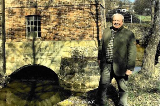 Bernd Wallters, rechts im Bild sammelt Wasserkraftwerke. Er steht vor einem historischen Backsteingebäude, einer Wasserkraftanlage über einem Kanal.