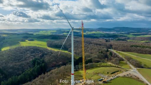 Windenergie-Anlage von Prokon vor Wald und wolkigem Himmel.