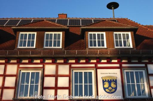 Die Fassade eines älteren Rathauses. Auf dem Dach eine Solarstrom-Anlage.