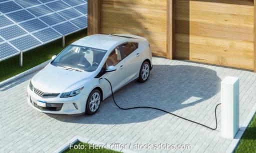 Ein E-Fahrzeug vor der Garage wird geladen mit PV-Anlage daneben.