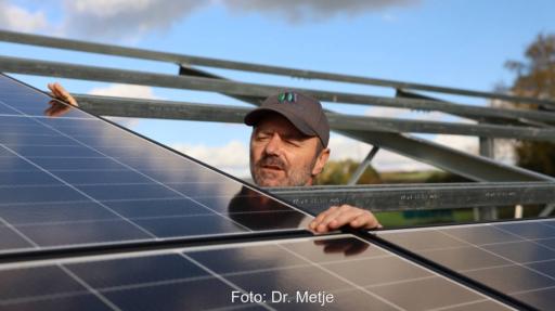 Installateuer lugt zwischen Solarmodulen hervor, die auf Unterkonstruktion ruhen.