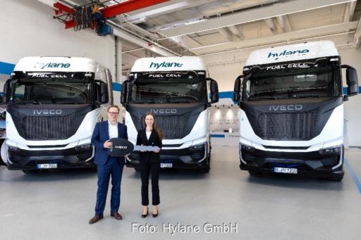 Christian Sulser (Vorstandsvorsitzender, Iveco Magirus AG) übergibt die Fahrzeuge an Dr. Sara Schiffer (Geschäftsführerin, Hylane GmbH). Im Hintergrund stehen die drei Sattelzugmaschinen.