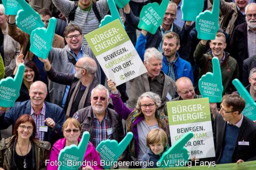 Gruppe von Menschen aus der Vogelperspektive demonstriert mit Pappschildern und überdimensionalen Schaumstoffhänden für Bürgerenergie, u.a. Energy Sharing.