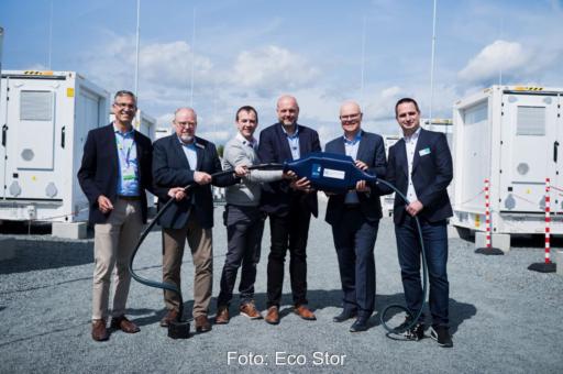 Sechs Personen halten einen überdimensionierten Stecker als Symbol für die Inbetriebnahme eines Großspeichers.