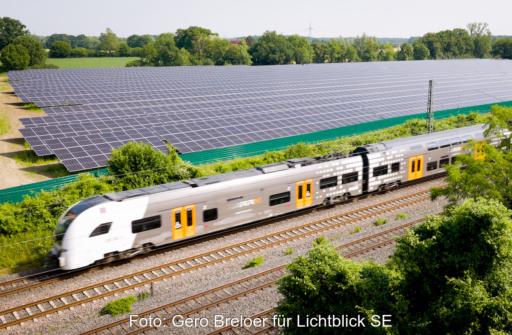 Blick von schräg oben auf den Solarpark an der Bahntrasse mit Zug im Vordergrund