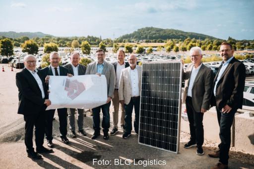 8 Männer mit Plan udn PV-Modul vor im Hintergrund stehenden Autos.