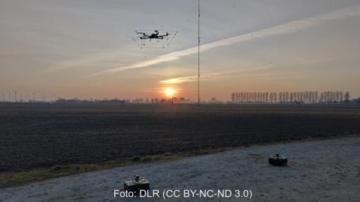 Eine Drohne startet zum Sonnenuntergang vor einer Windenergieanlage in den Himmel.