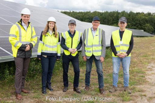 Fünf Personen stehen bei einer Einweihung in neongelben Warnwesten vor einem Solarmodul in einem Solarpark.