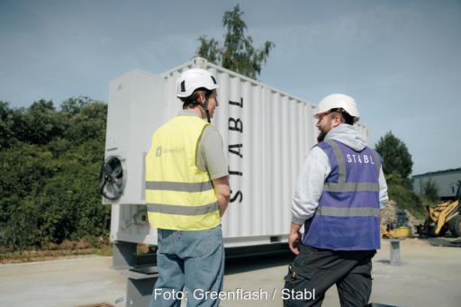 Zwei Personen stehen in Warnwesten und mit Baustellenhelm vor einer Speichereinheit.