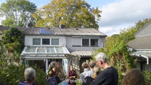 Menschengruppe von hinten im Garten eines Hauses mit kleiner PV-Anlage auf dem Dach: eine Solarparty.