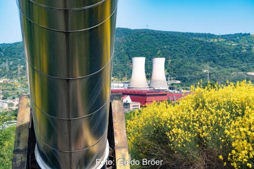 Blick auf ein Geothermie-Krafterk in Larderello. Im Vordergrund eine dicke Fernwärmeleitung und blühender Ginster.