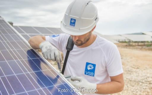 Mann mit VSB-Logo montiert Photovoltaik-Modul auf einer Freifläche.
