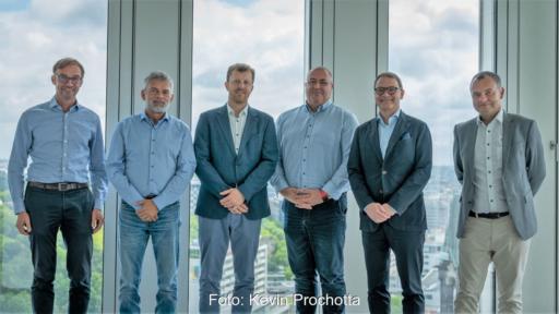 Sechs Männer im leichten Business-Outfit vor einem Fenster