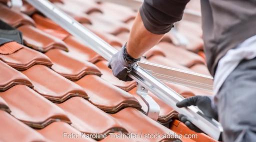 Die Hände eines Monteurs auf dem Dach halten eine Photovoltaik-Montageschiene, BDSH legt Fünf-Punkte-Plan für den Photovoltaik-Ausbau vor.