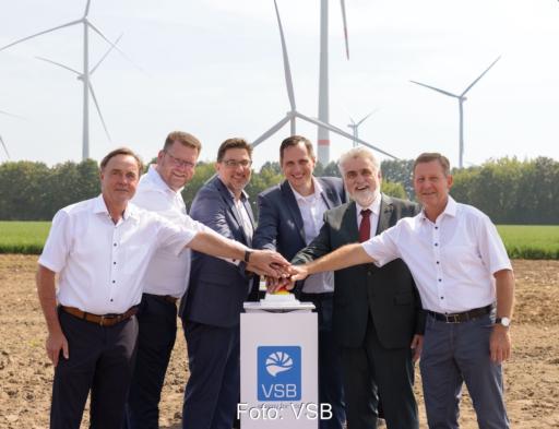 Bild von der Eröffnungsfeier: sechs Personen drücken symbolisch mit den Händen übereinander auf einen roten Knopf auf einem Sockel; im Hintergrund Windkraftanlagen.