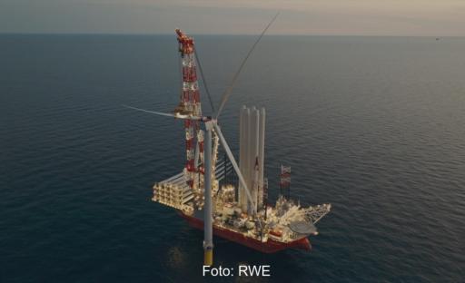 An einer Windkraftanlage liegt ein Schiff, um die Rotoren anzubringen.