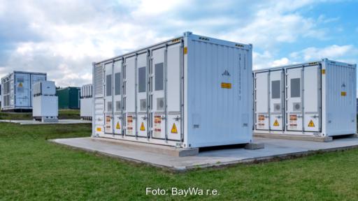Verschiedene Batteriespeichersysteme in Containern stehen neben und hintereinander auf Fundamenten im Rasen.