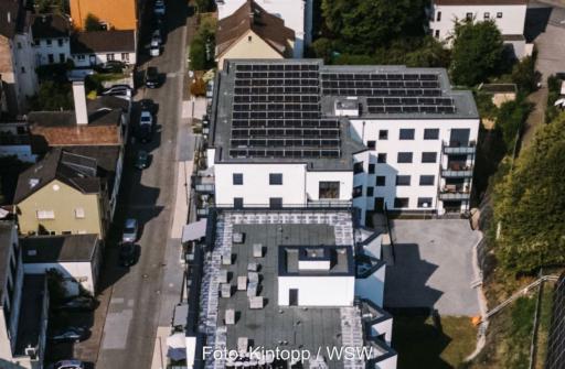Luftbild einer städtischen Wohnstraße mit einem Gebäude, das PV auf dem Flachdach installiert hat.