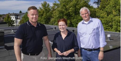 Eine Frau und zwei Männer auf einem Dach mit PV-Modulen.