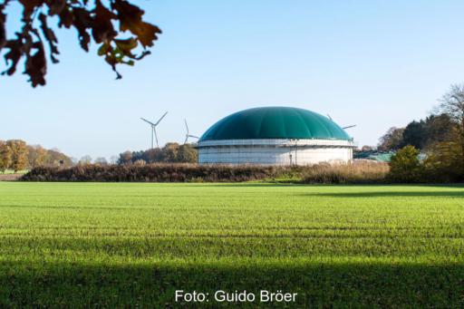 Biogasanlage in grüner Landschaft mit Windkraftanlagen im Hintergrund