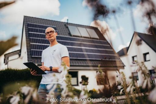 Ein Techniker mit einem Pad in der Hand vor einem Einfamilienhaus mit Dach-PV.