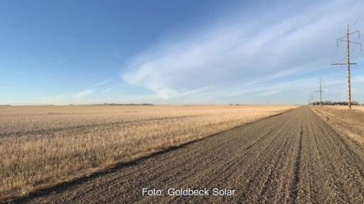 Zu sehen ist ein Acker unter blauem Himmel und ein Strommast - hier soll eine Photovoltaik-Anlage entstehen.