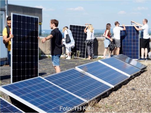 Personen arbeiten auf dem Flachdach eines Hochhauses an Steckersolaranlagen.