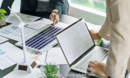 Zwei Personen an einem Tisch mit Laptop, Windradmodell und PV-Modell, der Wirtschaftlichkeitsrechner für Home Energy Management Systeme von Energielenker berechnet Szenarien.