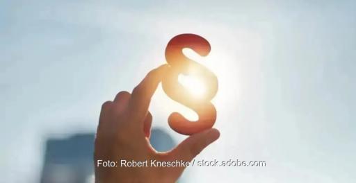 Eine Hand hält ein Paragrafenzeichen in die Sonne.