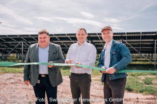 Drei Personen stehen vor einem Freiflächenmodul im Hintergrund und schneiden ein grün-weißes Band durch.