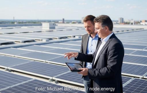Zwei Personen stehen auf einer Dachfläche mit Photovoltaik-Modulen. Einer hält ein Tablet in der Hand, auf das beide schauen.