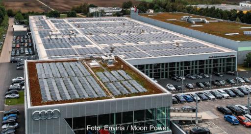 Aufsicht auf das Dach einer Gewerbehalle mit Audi-Logo, den vier Ringen an der Seite; auf der vorderen Dachfläche ist eine PV-Anlage zu sehen.