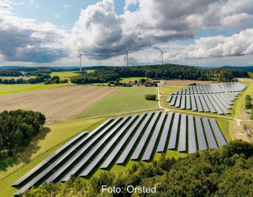 PV-Freifläche mit drei Windenergieanlagen im Hintergrund.