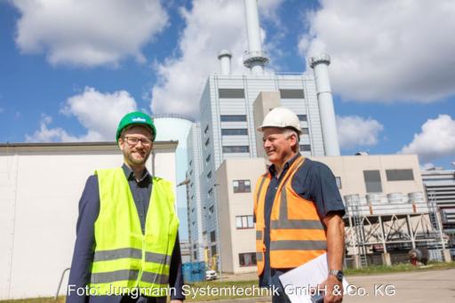 Zwei Männer in Sicherheitswesten und Helmen vor einem Heizkraftwerk.