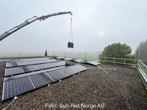 Ein Kran hebt faltbare PV-Module auf ein Flachdach.